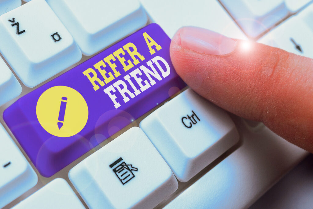 A keyboard with a button that says "Refer a Friend". A person's finger is about to push it.